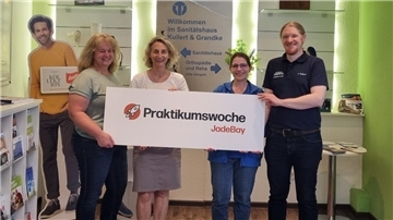 Zwei Männer und zwei Frauen halten ein Plakat mit der Aufschrift "Praktikumswoche JadeBay" in die Kamera.