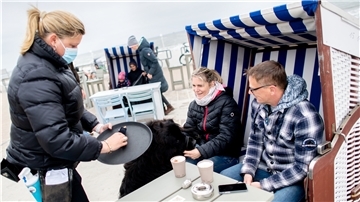 Kellnerin Nina bedient Anett und Christoph aus der Nähe von Oldenburg, die mit ihrem Hund Murphy in einem Strandkorb auf Norderney vor dem Surfcafe an der Strandpromenade sitzen. Ab sofort sind auch Nicht-Niedersachsen als Urlauber willkommen.