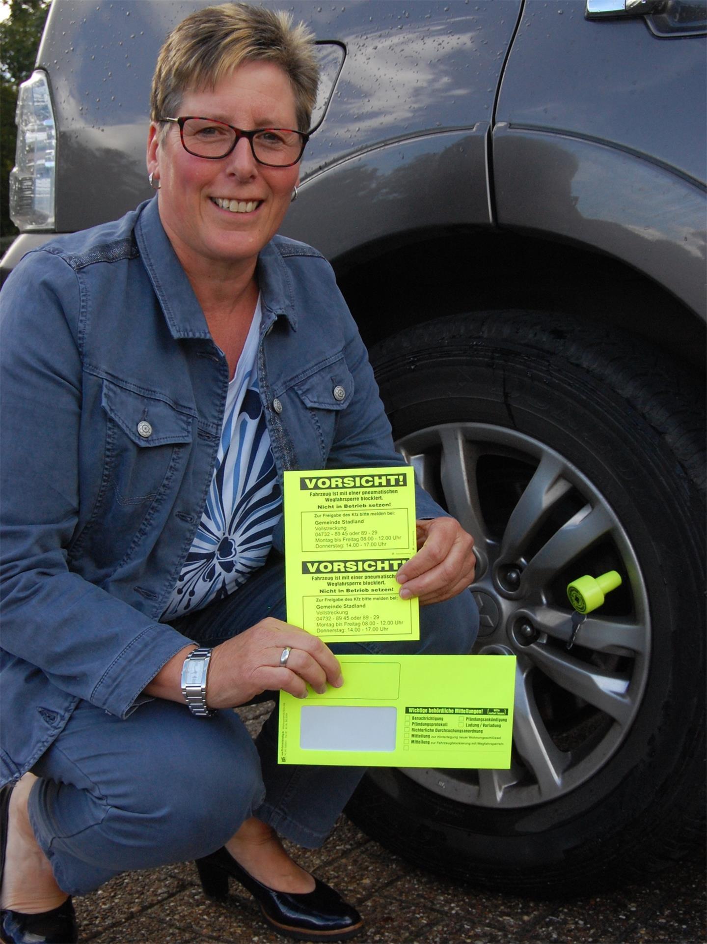 Kerstin Hullmann ist die Vollstreckerin der Gemeinde Stadland. Sie zeigt den Ventilwächter, der auf den Reifen gesetzt wird, sowie die Warnaufkleber und den gelben Brief, den säumige Zahler erhalten.
