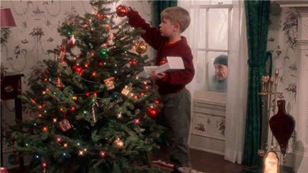Ein Junge schmückt einen Weihnachtsbaum und wird beobachtet.