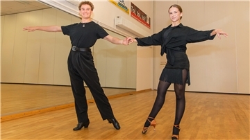Ein junges Latein-Tanzpaar in einer Tanzpose auf dem Parkett vor einem großen Spiegel.
