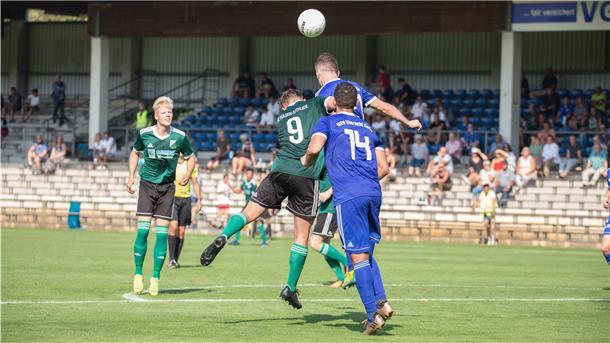 Sechs Männer stehen in Trikots auf dem Fußballplatz.