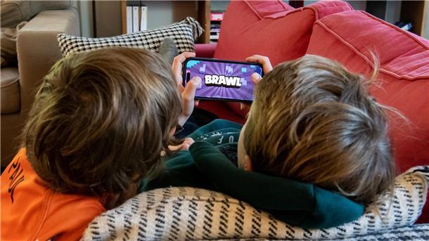 Zwei Jungen liegen zusammen auf dem Sofa und spielen das Online-Spiel "Brawl Stars" auf einem Smartphone.  Kinder und Jugendliche verbringen viel Zeit mit Videospielen. Wenn Eltern richtif´g damit umgehen, können sie schädliche Folgen verhindern.