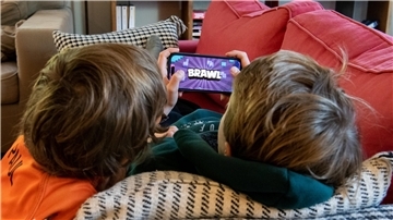 Zwei Jungen liegen zusammen auf dem Sofa und spielen das Online-Spiel "Brawl Stars" auf einem Smartphone.  Kinder und Jugendliche verbringen viel Zeit mit Videospielen. Wenn Eltern richtif´g damit umgehen, können sie schädliche Folgen verhindern.