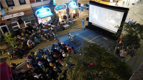 Zahlreiche Menschen sitzen abends auf Klappstühlen und Sofas vor einer großen Leinwand bei einem Open-Air-Kino in der Alten Bürger in Bremerhaven.