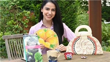 Eine junge Frau mit schwarzen Haaren sitzt an einem Tisch. Auf dem Tisch liegen ein Paket Kaffee, eine Tasche und andere handgearbeitete Dinge.