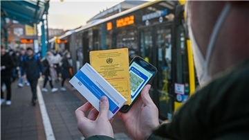 Ein Mann hält einen Corona-Schnelltest, seinen Impfausweis und ein Handy in der Hand.