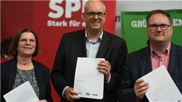 Kristina Vogt (Linke,), Andreas Bovenschulte (SPD) und Björn Fecker (Bündnis 90/Die Grünen) halten den Koalitionsvertrag in der Hand. 