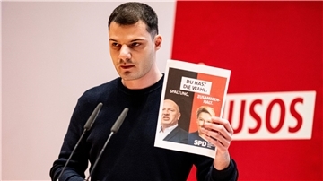 Kubilay Yalcin hält auf der Landesdelegiertenkonferenz der Jusos Berlin ein Wahlplakat mit Giffey und Wegner in die Höhe.
