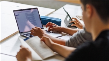  Schüler sitzen vor einem Computer und benutzen ein KI-Tool. 