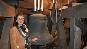 Frau steht neben einer alten Glocke.
