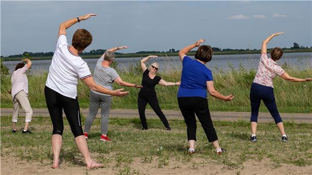 Frauen machen am Strand eine Qigong-Übung.