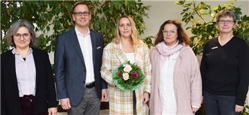 Vier Frauen und ein Mann stehen nebeneinander. Die Frau in der Mitte hält einen Blumenstrauß in einer Hand.