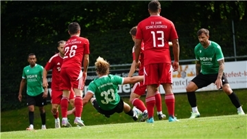 Fußballer in roten und grünen Trikots kämpfen auf dem Platz um den Ball.