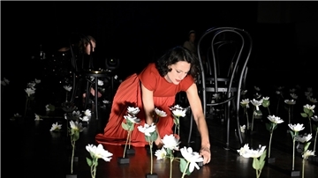 Schauspielerin in einem roten Kleid und Blumen auf einer Bühne, kniend