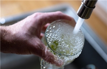 Tinkwasser läuft aus dem Wasserhahn in einer Küche in ein Glas