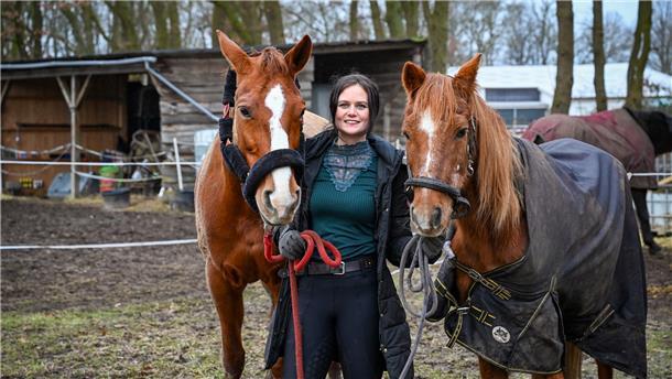 Eine Reiterin mit zwei Pferden steht auf einem Hof.
