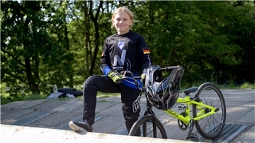 Ein Mädchen steht mit ihrem BMX-Rad am Starthügel.