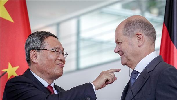 Li Qiang (l) zeigt zum Ende des Pressestatements auf den Kopfhörer für die Übersetzung im Ohr von Bundeskanzler Olaf Scholz.
