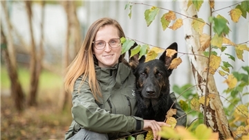 Eine Frau mit ihrem Hund hinter Blättern. 