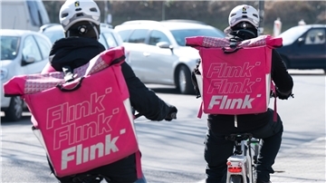 Zwei Fahrradkuriere tragen Rucksäcke mit dem Logo des Lebensmittel Lieferdienstes Flink.