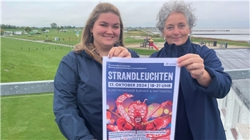 Zwei Frauen mit einem Plakat am Burhaver Strand. Lisa Schlesies-Janssen und Sabine Schmidt von Tourismus-Service Butjadingen.