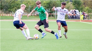 Ein Fußballer nimmt es mit zwei Gegenspielern auf.  