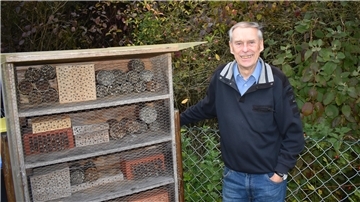 Ein älterer Mann steht neben einem Stand mit Insektennisthilfen.