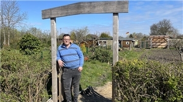 Mann in Torbogen vor Schrebergarten.