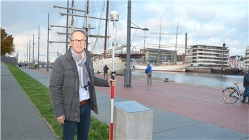 Marc Kewes steht mit einem Vermessungsstab am GPS-Referenzpunkt, den das Vermessungs- und Katasteramt am Neuen Hafen in Bremerhaven eingerichtet hat.