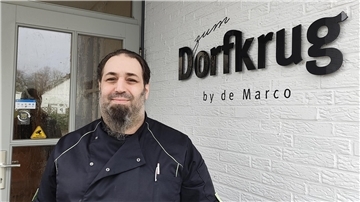 Ein Mann in Kochkleidung steht vor einem Restaurant.