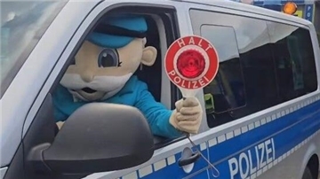 Eine Figur sitzt in einem Polizeiauto und hält eine Kelle mit der Aufschrift "Halt Polizei" in der Hand.