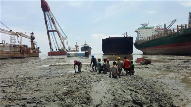 Arbeiter stehen bis zur Hüfte in Matsch und Müll beim Abwracken von Schiffen in Bangladesch