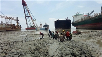 Arbeiter stehen bis zur Hüfte in Matsch und Müll beim Abwracken von Schiffen in Bangladesch