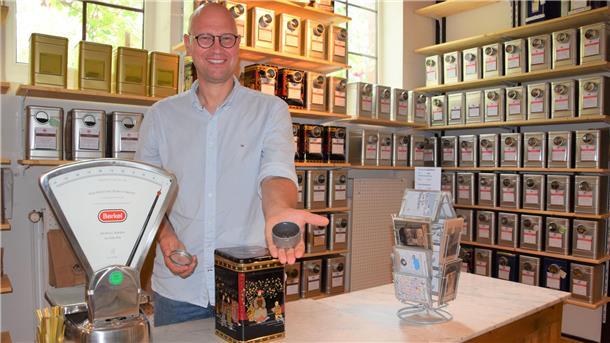Ein Mann steht hinter seinem Verkaufstresen. Er präsentiert in seiner linken Hand den Tee, den er im Teekontor in Butjadingen verkauft. 