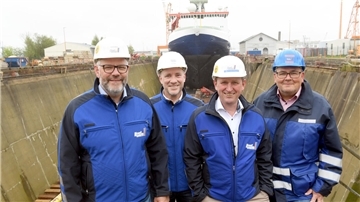 Vier Männer stehen vor einem Schiff in einem Dock. 