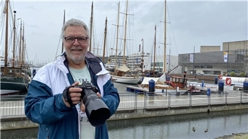 Ein Mann steht vor einem Hafen und hält eine Kamera in den Händen.