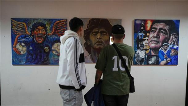 Menschen betrachten eine Kunstausstellung mit Bildern des verstorbenen Fußballstars Maradona.