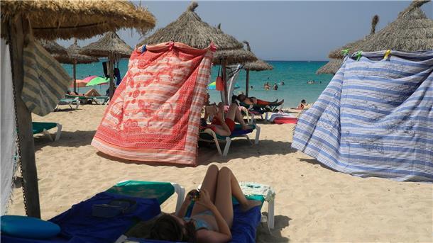 „Hält man nicht mehr aus“: Hitze plagt Touristen-Hotspots Menschen schützen sich bei extremer Hitze mit Strandtüchern vor der Sonne am Strand von Arenal.