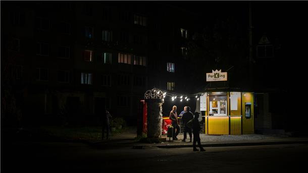 Ukraine warnt: Neue Fluchtbewegungen wegen Energie-Ausfällen Menschen stehen an einer Straße vor einer beleuchteten Bar. In der Ukraine greift Russland weiter gezielt Kraftwerke und andere Infrastruktur an.