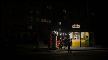 Menschen stehen an einer Straße vor einer beleuchteten Bar. In der Ukraine greift Russland weiter gezielt Kraftwerke und andere Infrastruktur an.