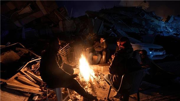 Antakya - die Stadt, die es nicht mehr gibt Menschen wärmen sich an einem Feuer vor zerstörten Gebäuden.