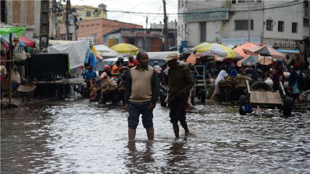 Menschen waten durch das Hochwasser einer überfluteten Straße in Antananarivo.