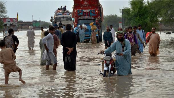 Menschen waten im August 2022 im pakistanischen Nasirabad durch auf einer überschwemmten Straße durchs Hochwasser.