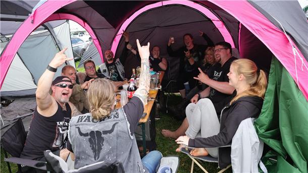 Metal-Fans aus Kiel feiern auf einem Zeltplatz auf dem vom Regen aufgeweichten Festivalgelände.