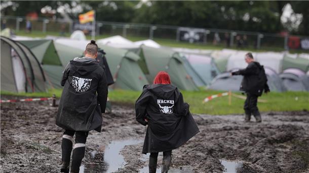 Metal-Fans sind auf dem schlammigen Festivalgelände unterwegs.