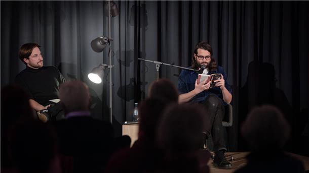 Michel Decar (rechts) stellt den Zuhörern am vierten Abend der Literarischen Wochen den Taugenichts vor, der in dem satirischen Künstlerroman „Kapitulation“ das Schreiben aufgeben will. Da hört nicht nur Tobias Pollok, der Kulturreferent der Arbeitnehmerkammer, aufmerksam zu.