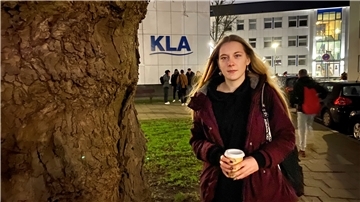 Ein Mädchen mit roter Jacke steht mit einem Kaffeebecher neben dem Baum vor der KLA in Bremerhaven.