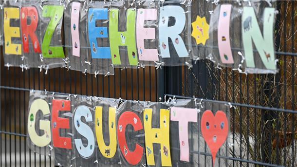 Mit bunten Buchstaben sind die Worte „Erzieher*in gesucht“ geformt, die an einem Zaun einer Kindertagesstätte befestigt sind. Städte und Gemeinden suchen derzeit händeringend Personal. So auch in Breddorf.