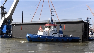Ein Schleusentor wird mithilfe eines Schwimmkrans aus dem Dock gehoben. Im Vordergrund zieht der Schlepper „Fairplay 53“ das massive Stahlbauwerk über das Hafenbecken. 